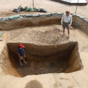 Archaeologists stand around deep excavation unit