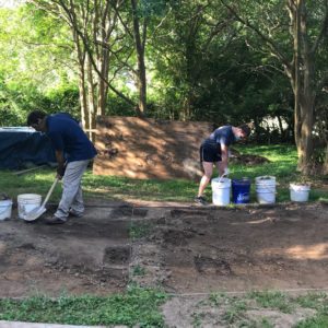 Archaeologists excavating in front of trees