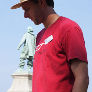 Archaeologist standing in front of a statue and looking down at an item off-camera