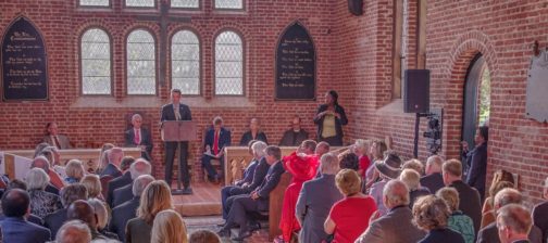 Speaker at podium talks to seated group in brick church