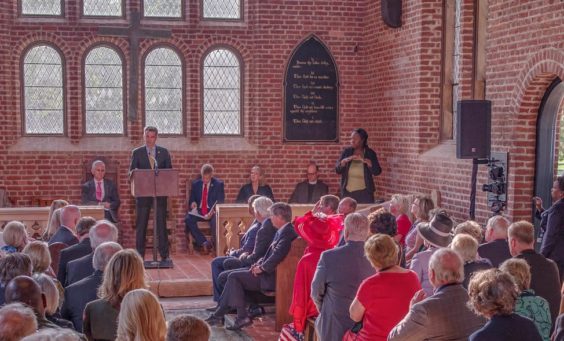 Speaker at podium talks to seated group in brick church