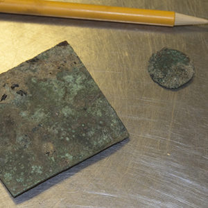 copper square, jetton, and musket ball next to a pencil for scale