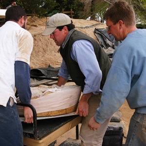 three men carrying a wooden tray with a block of soil and embedded iron armor piece