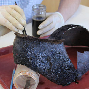 conservator applying solution to a corroded close helmet on a tray