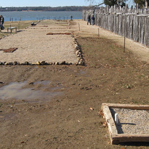 Square feature outlined with wooden beams and filled with gravel with additional long rectangular features outlined by cobblestones and gravel in the background