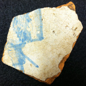 fragment of a delft tile with corner of a blue decoration of a gentleman wearing boots and a cape