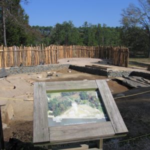 Sign with image of digitally-reconstructed James fort buildings in front of excavation unit and palisade