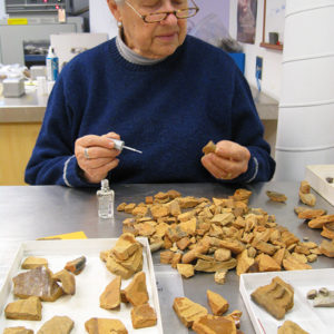 A woman using a small brush to paint ceramic sherds with B-72