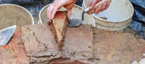 A person removes a wedge-shaped brick from the brick well ring