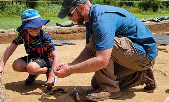 Senior Staff Archaeologist Sean Romo instructs a camper on the troweling process.