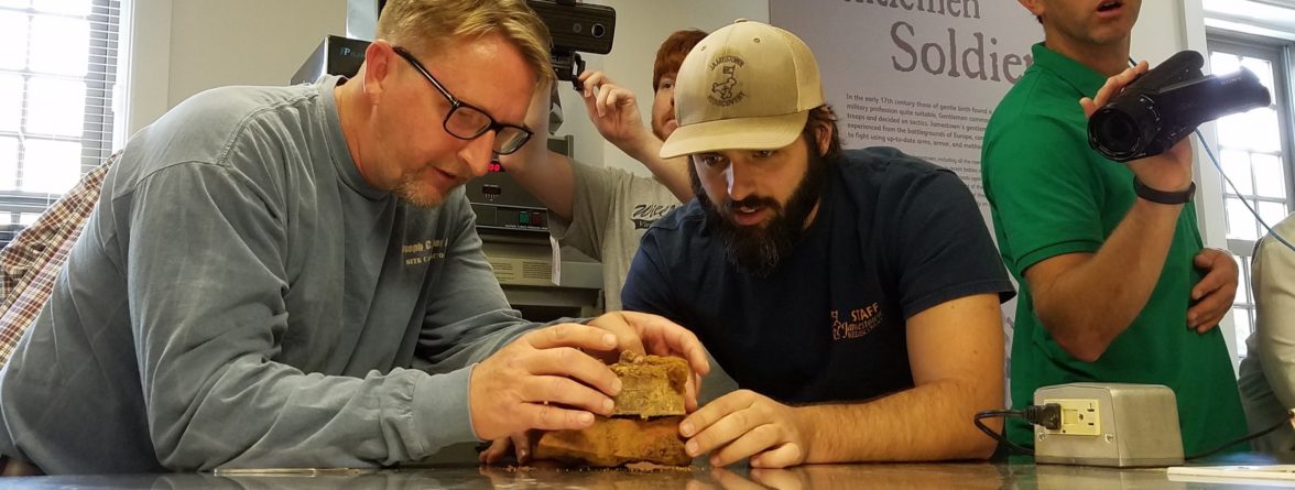 Staff examine artifact on lab table while others film