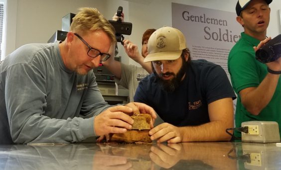 Staff examine artifact on lab table while others film