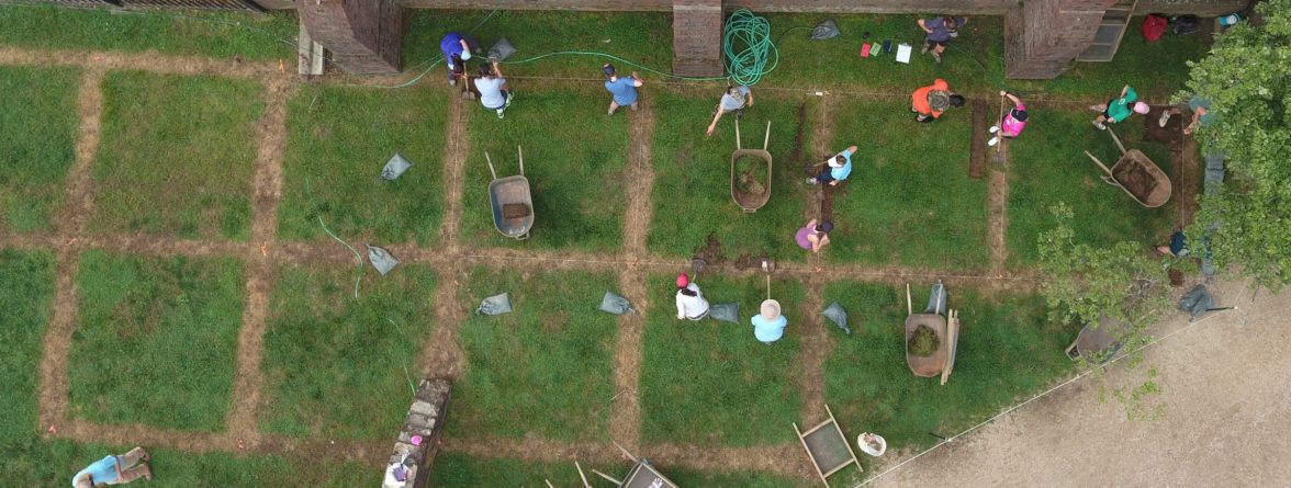 Aerial view of wheelbarrows and students shoveling in square excavation units