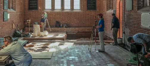 Archaeologists recording the location of excavated features within the floor of a brick church