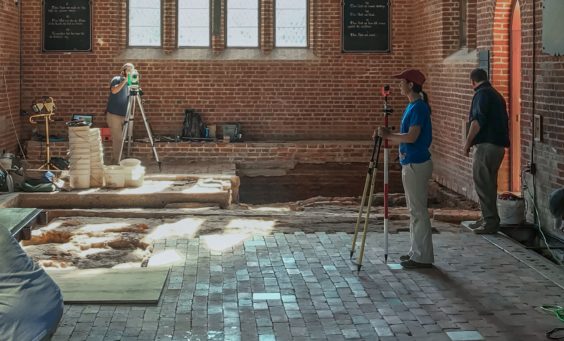 Archaeologists recording the location of excavated features within the floor of a brick church